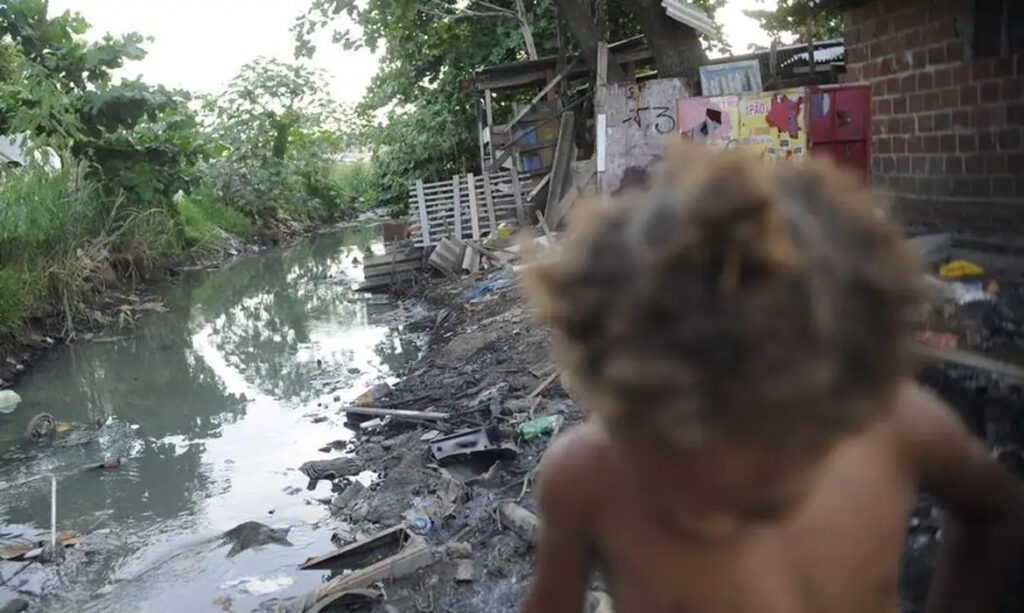 Imagem de riacho com falta de saneamento básico e uma criança passando em favela do Complexo da Maré - (foto: Arquivo/ Fernando Frazão/ Agência Brasil)